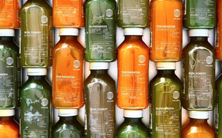 Viele DALUMA Saftflaschen in Grün und Orange dicht nebeneinander gestapelt, mit den Sorten SUPERGREEN, RUN, FOREST und THE RADIATOR