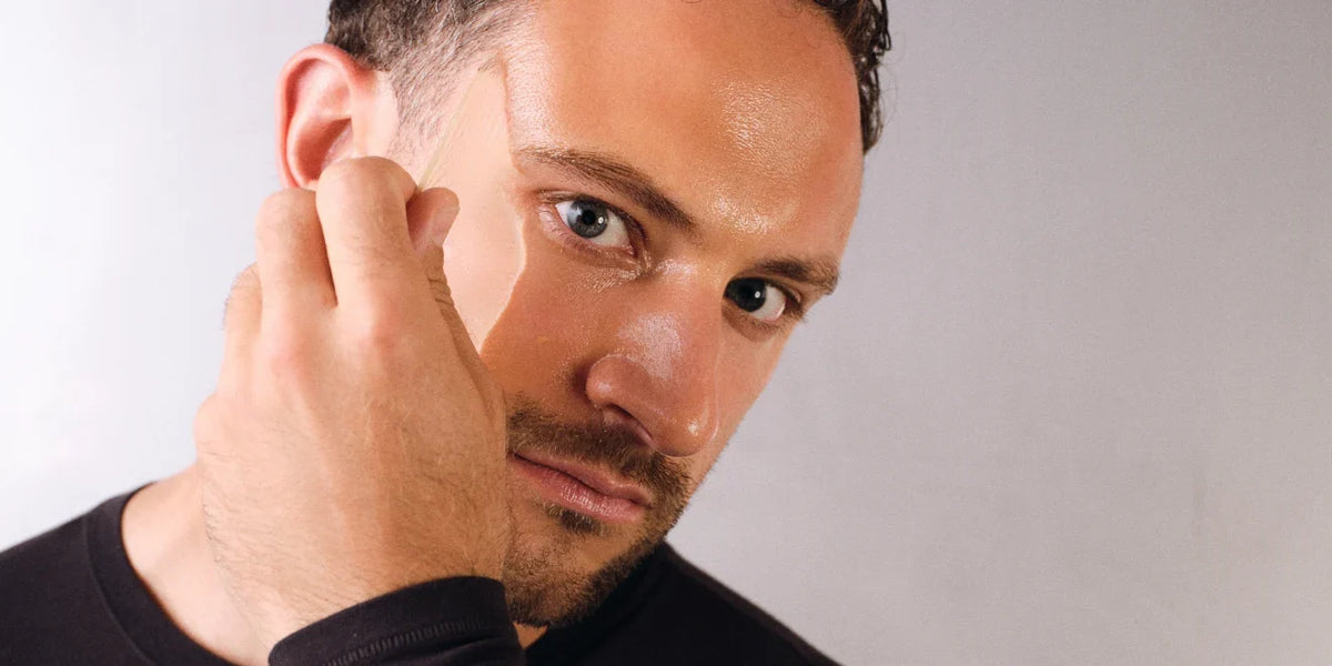 Mann zieht eine transparente Gelmaske von Stirn und Wange ab und blickt direkt in die Kamera, heller grauer Hintergrund