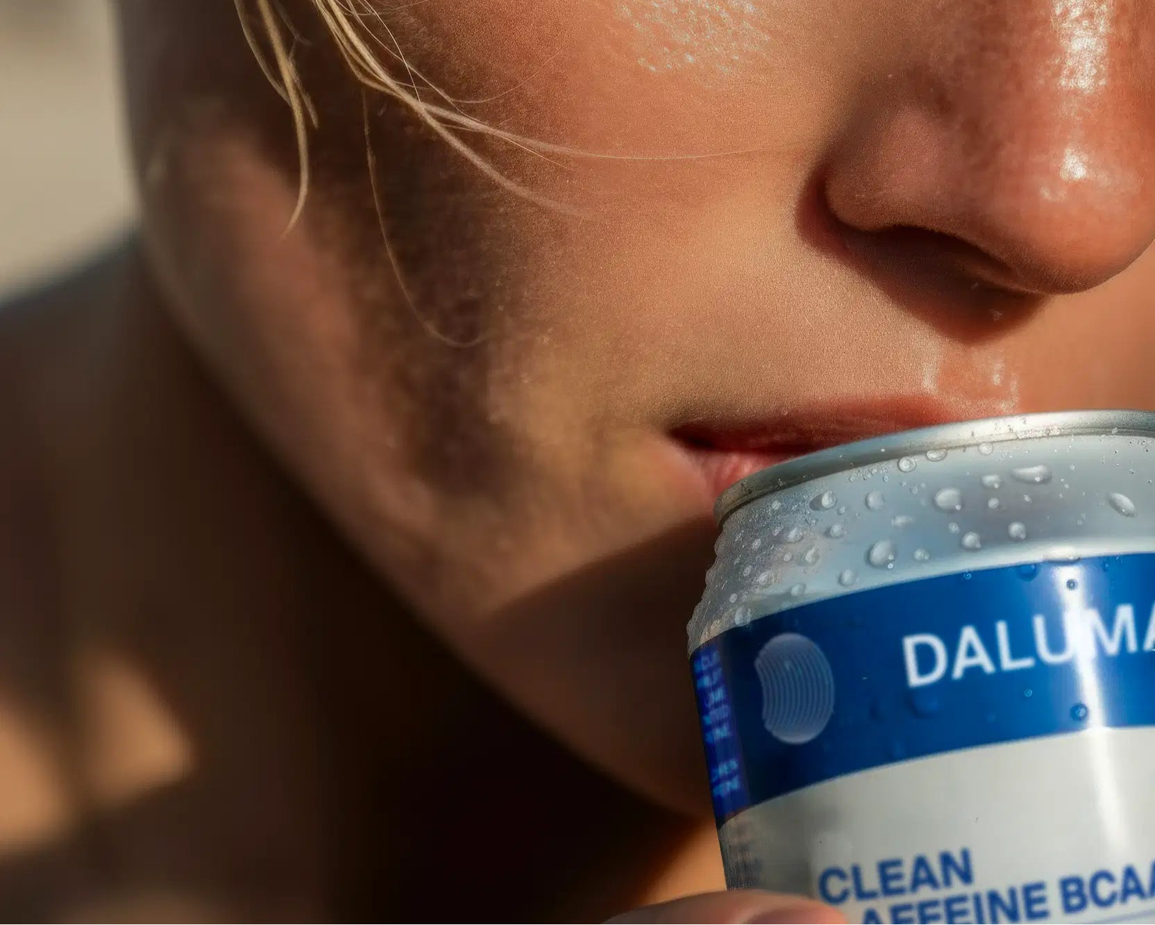 Nahaufnahme einer Person, die eine blau-weiße Dose DALUMA CLEAN BCAA ENERGY DRINK an die Lippen hält, um einen Schluck zu nehmen. Die mit Wasser gefüllte Dose hebt grünen Kaffee als eine der erfrischenden Zutaten hervor.