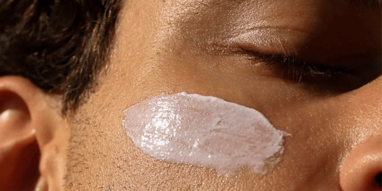 Eine Nahaufnahme des Gesichts einer Person mit geschlossenen Augen, auf deren Wange eine dicke Schicht weißer Creme oder Lotion aufgetragen ist.