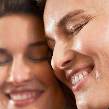 Eine Nahaufnahme einer lächelnden Person mit klarer Haut neben einer spiegelnden Oberfläche, deren strahlendes Aussehen in beiden Bildern zu sehen ist - dank Hautregeneration unterstützt durch SIX ELEMENTS SKIN KOLLAGEN KAPSELN von DALUMA.