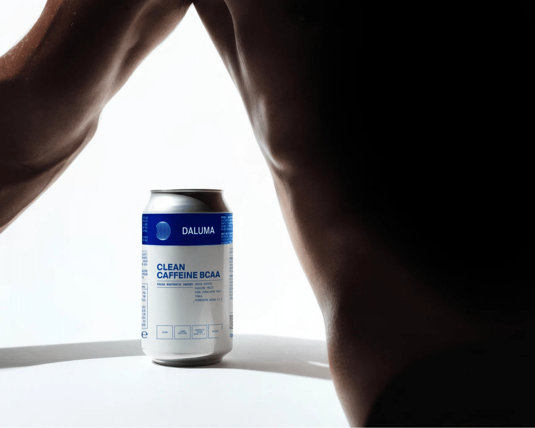 Eine Dose DALUMA CLEAN BCAA ENERGY DRINK 24 PACK steht auf einer weißen Fläche, umrahmt vom Arm und Oberkörper einer dunkelhäutigen Person - teilweise im Schatten vor einem hellen Hintergrund.