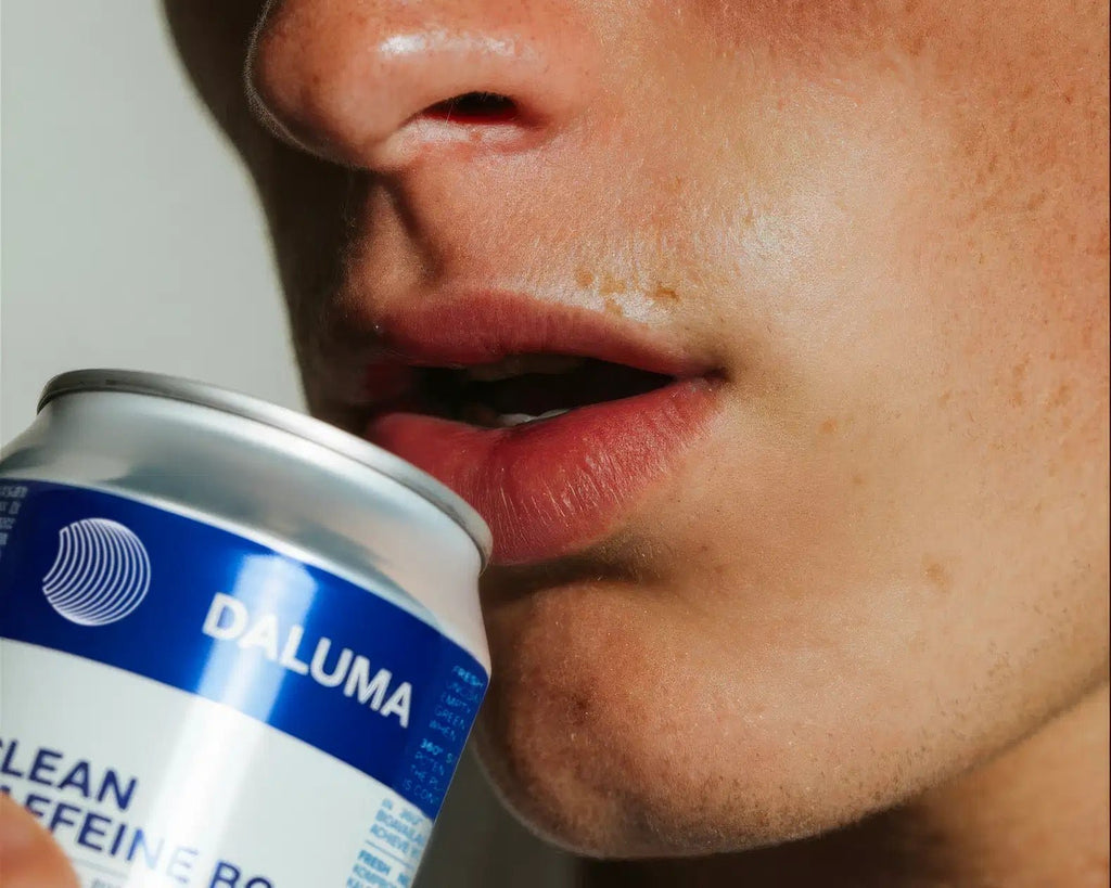 Eine Nahaufnahme zeigt eine Person, die eine geöffnete Dose DALUMA ENERGY & BALANCE DUO an ihre Lippen hält. Auf dem blau-weißen Etikett steht "natürliche Energie", und der Mund der Person ist leicht geöffnet, bereit, einen Schluck zu nehmen.