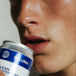 Nahaufnahme des Gesichts einer Person, die eine blau-weiße Dose DALUMA CLEAN BCAA ENERGY DRINK an den Mund hält, um einen Schluck aus dem 24er-Pack des Energydrinks mit natürlichem Koffein zu nehmen, mit Schwerpunkt auf Lippen und Nase.