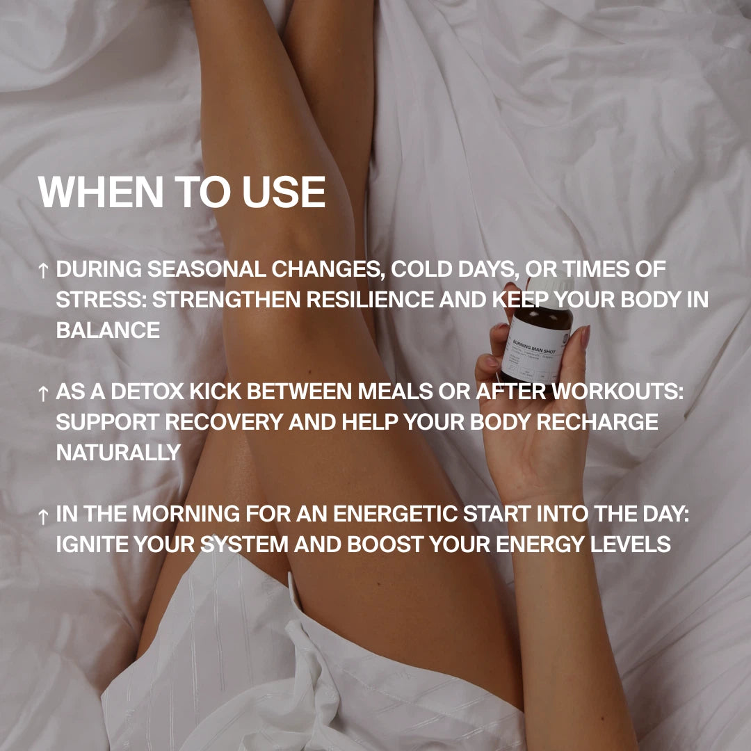 Eine Person sitzt auf einem weißen Bett und hält eine Flasche DALUMA BURNING MAN INGWERSHOT 24 PACK. Anwendungstipps: Genießen Sie es während der jahreszeitlichen Veränderungen, als Entgiftung zwischen den Mahlzeiten oder nach dem Training, und am Morgen für Energie und Ausgeglichenheit.