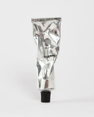 Eine zerknitterte silberne Tube mit schwarzer Kappe, auf der FACIAL MOISTURIZER GESICHTSPFLEGE und DALUMA steht, ruht auf einem schlichten weißen Hintergrund - eine elegante Feuchtigkeitscreme für das Gesicht und natürliche Feuchtigkeitscreme für jeden Hauttyp.