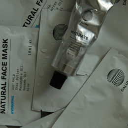 Eine Tube mit der Aufschrift HYDRATING ESSENTIALS ruht auf einer weißen Verpackung mit der Aufschrift DALUMA, auf der Wassertropfen sichtbar sind.