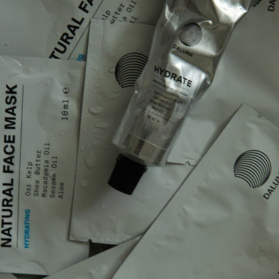 Eine Tube mit der Aufschrift HYDRATING ESSENTIALS ruht auf einer weißen Verpackung mit der Aufschrift DALUMA, auf der Wassertropfen sichtbar sind.
