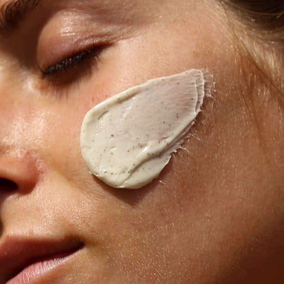 Eine Nahaufnahme des Gesichts einer Person mit geschlossenen Augen, auf der das 2x MASK BUNDLE von DALUMA zu sehen ist. Eine glatte, dicke Schicht der beigen Maske mit einigen Tupfen wird auf die Wange aufgetragen und verleiht der Haut ein gesundes Aussehen.