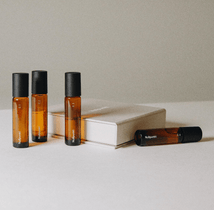 Die Nullpunkt Complete Collection besteht aus vier Braunglas-Rollerflaschen mit schwarzen Verschlüssen, die neben einem geschlossenen beigen Buch auf einem minimalistischen, neutralen Hintergrund angeordnet sind.