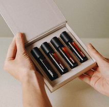 Eine Person hält eine geöffnete Schachtel in der Hand, die die NULLPUNKT COMPLETE COLLECTION von Nullpunkt enthält - vier kleine Braunglasfläschchen mit schwarzen Verschlüssen, fein säuberlich angeordnet in einem hellen, gepolsterten Organizer.