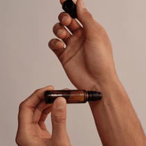 Vor einem neutralen Hintergrund hält eine Person einen kleinen Braunglas-Roll-on-Flakon aus der Nullpunkt Complete Collection von Nullpunkt und entfernt mit der anderen Hand vorsichtig die schwarze Kappe.