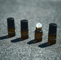 Vier kleine bernsteinfarbene Fläschchen mit schwarzem Verschluss aus dem Nullpunkt NULLPUNKT DISCOVERY SET sind auf einer grauen Fläche angeordnet. Ein Fläschchen ohne Deckel offenbart einen weißen Rollerball. Die Etiketten Relieve, Release und Refocus deuten auf wohltuende Aromatherapie-Mischungen hin.