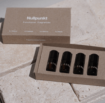 Eine Pappschachtel mit der Aufschrift NULLPUNKT DISCOVERY SET von Nullpunkt enthält vier kleine, dunkle Glasflaschen - 0,1, 0,2, 0,3 und 0,4 -, die ordentlich auf einer hellen Steinoberfläche angeordnet sind.