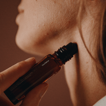 Nahaufnahme einer Person, die sich das Serum Nullpunkt GRADE 0.2 RELEASE aus einer braunen Glasflasche mit einer Pipette in den Hals eintropft. Der Hintergrund ist sanft verschwommen.