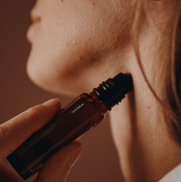 Nahaufnahme einer Person, die sich das Serum Nullpunkt GRADE 0.2 RELEASE aus einer braunen Glasflasche mit einer Pipette in den Hals eintropft. Der Hintergrund ist sanft verschwommen.