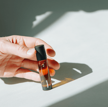 Eine Hand hält ein kleines Braunglas-Tropffläschchen mit der Aufschrift NULLPUNKT GRADE 0.3 REFOCUS von Nullpunkt und einer schwarzen Kappe, die einen weichen Schatten auf eine weiße Fläche in hellem Tageslicht wirft.