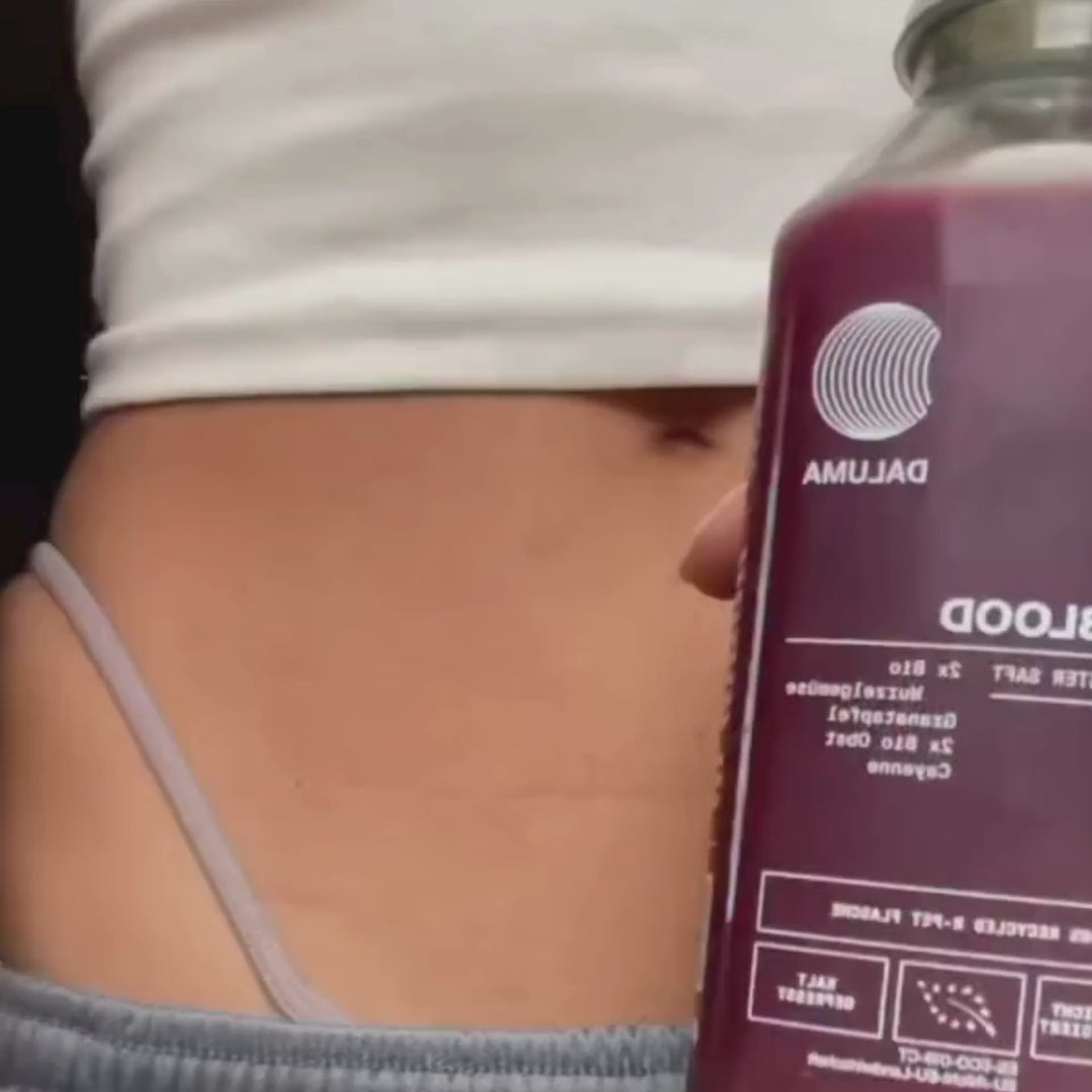 Nahaufnahme des Unterleibs einer Person in einem hellvioletten Hosenbund, die eine mit violetter Flüssigkeit gefüllte Flasche Daluma BETTER SHAPE SAFTKUR 3 TAGE Saft hält.