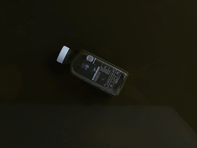 Eine dunkle Saftflasche mit weißem Deckel und schwarzem Etikett schwimmt schräg auf einer glatten, dunklen Oberfläche. Das Etikett enthält Text und Nährwertangaben.